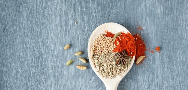 A collection of vibrant spices displayed on a wooden spoon against a textured background.