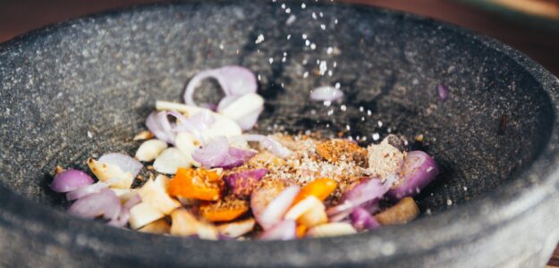 Close-up of seasoning being added to fresh ingredients in a stone bowl, perfect for culinary themes.