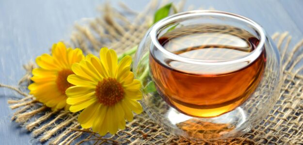 Glass cup of herbal tea with yellow flowers on a textured background.