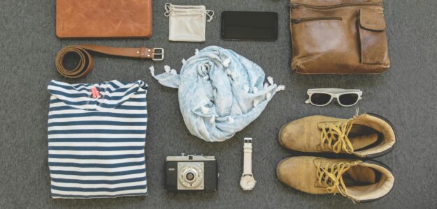 Vintage travel essentials flat lay with leather bags, shoes, camera, and clothing.