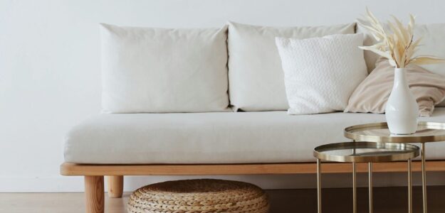 A chic minimalist living room featuring a white sofa with cushions, dried flowers in a vase, and a wooden floor.